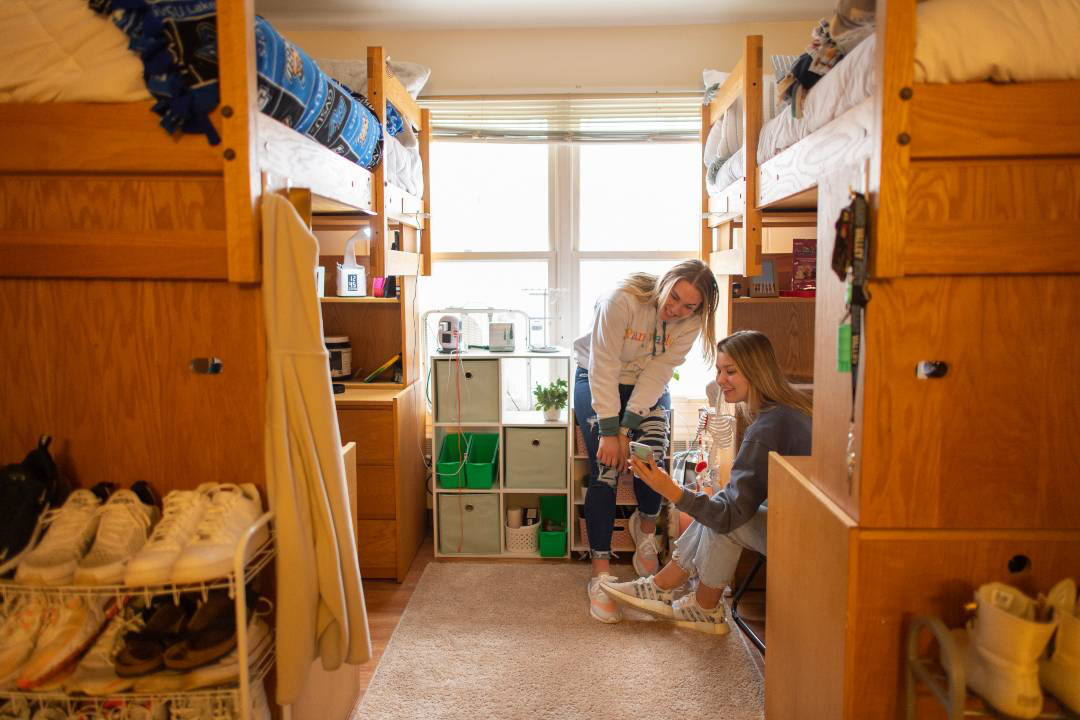 Two people in a suite style room with lofted beds and wooden furniture, sitting and smiling near a window, creating a warm, friendly atmosphere.
